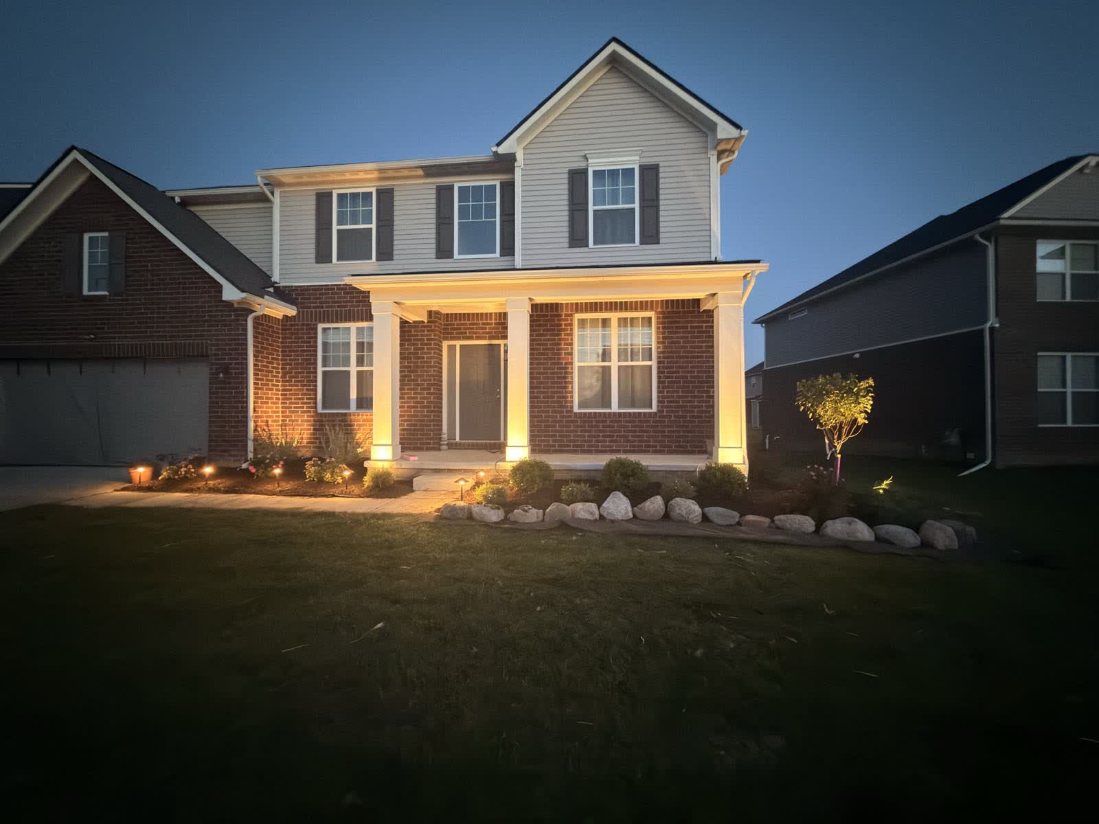 The finished front yard at dusk with low-voltage landscape lighting on the porch columns and path lights through the bed